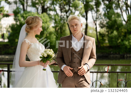 Couple poses by the water during a wedding celebration in a green park Couple poses by the water during a wedding celebration in a green park 132324405