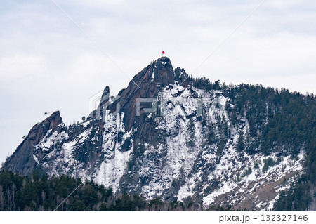 A majestic rock with a red flag on the mountaintop. 132327146