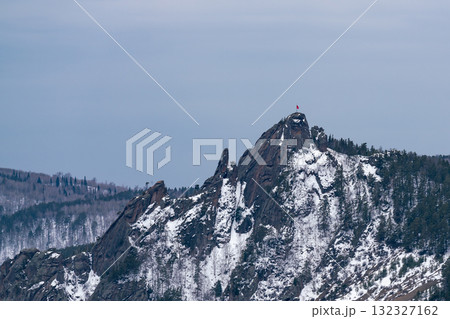 A majestic rock with a red flag on the mountaintop. 132327162