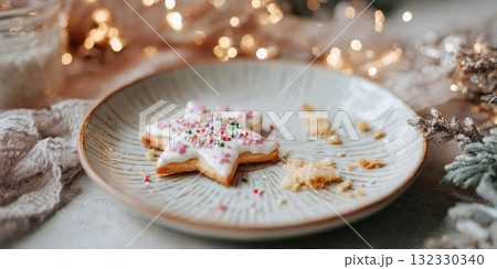 An empty ceramic plate holds a single decorated cookie, surrounded by holiday lights and festive decorations during Christmas 132330340
