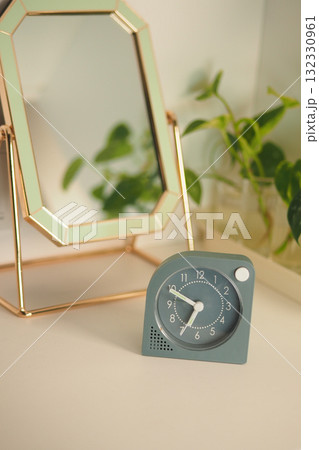 Modern clock displayed on a desk near a plant and mirror Modern clock displayed on a desk near a plant and mirror 132330961