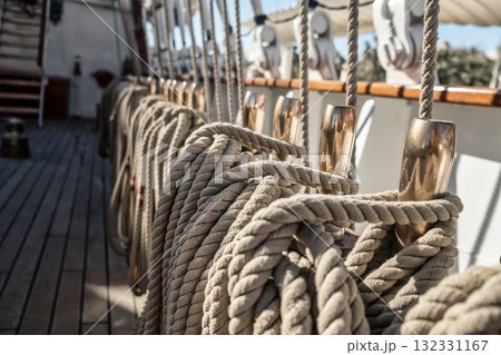 Neatly coiled ropes on the deck of a traditional sailing ship, resting on polished metallic pins. Classic maritime scene depicting organized sail rigging Neatly coiled ropes on the deck of a traditional sailing ship, resting on polished metallic pins. Classic maritime scene depicting organized sail rigging 132331167