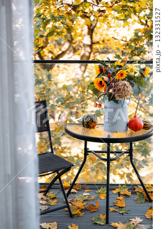 Seasonal floral arrangement in a vintage can on balcony table with gourds, leaves, and a black chair in soft natural light. Micro-retreats, flower therapy, mental wellness, mindful balcony design 132331527