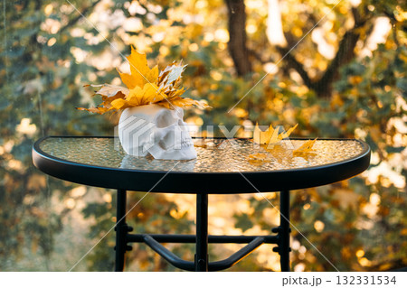 White skull with yellow maple leaves on top, placed on a glass table with soft autumn light and blurred background. Visual metaphor for cognitive health and awareness, brain health, memory symbolism White skull with yellow maple leaves on top, placed on a glass table with soft autumn light and blurred background. Visual metaphor for cognitive health and awareness, brain health, memory symbolism 132331534