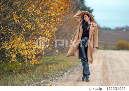 Portrait of a beautiful young brunette woman in coat and hat on a country road Portrait of a beautiful young brunette woman in coat and hat on a country road 132331963