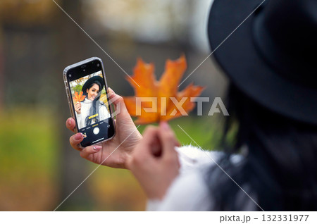 woman in hat taking selfie with smartphone with autumn leaves in the park woman in hat taking selfie with smartphone with autumn leaves in the park 132331977