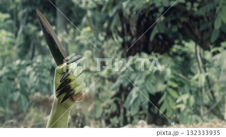 Witch hand with a long black nail holding a knife with a haunted forest background. Zombie, devil, evil, satan, or monster hand. Concept of Spooky Halloween 132333935