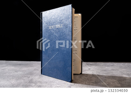 Blue book of the Holy bible. Standing on the table with a dark background. Symbol of faith in God. Concept of Spirituality, Christianity, religion, faith, Jesus, or belief Blue book of the Holy bible. Standing on the table with a dark background. Symbol of faith in God. Concept of Spirituality, Christianity, religion, faith, Jesus, or belief 132334030
