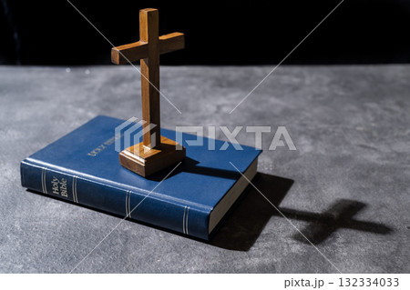 Blue book of the Holy bible and Christian cross. Standing on the table with a dark background. Symbol of faith in God. Concept of Spirituality, Christianity, religion, faith, Jesus, or belief 132334033