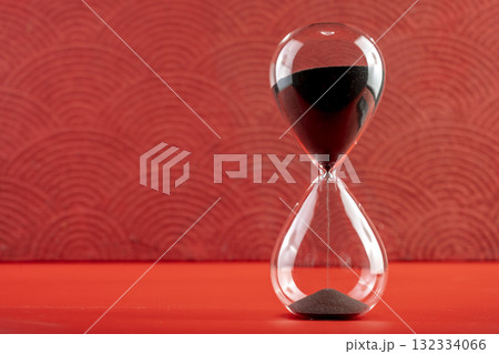 Hourglass with black sand on a red background. Time passing or time flowing. Sand glass, sand timer, sand clock. Concept of time 132334066