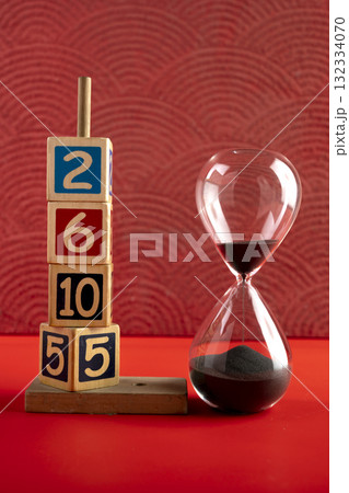 Hourglass with black sand with a wooden number block on a red background. Time passing or time flowing. Sand glass, sand timer, sand clock. Concept of time Hourglass with black sand with a wooden number block on a red background. Time passing or time flowing. Sand glass, sand timer, sand clock. Concept of time 132334070
