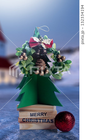 Paper Christmas tree with a wreath, bells, and bow. Merry Christmas greeting on wooden blocks with a Christmas ornament. Holiday greetings or winter themes. Concept of the Merry Christmas celebration 132334194