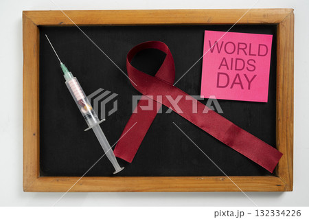 Red ribbon and syringe with chalkboard with the text of World Aids Day on the note. Symbolizing awareness and support for HIV or AIDS patients. Mockup or Copy space. Concept of Healthcare and Medicine 132334226