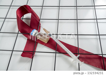 Red ribbon and syringe with vial on a white background. Symbolizing awareness and support for HIV or AIDS patients. World Aids Day. Concept of Healthcare and Medicine 132334231