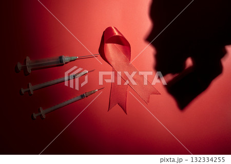 Red ribbon and syringe with silhouette of human head skull on a red background. Symbolizing awareness and support for HIV or AIDS patients. World Aids Day. Concept of Healthcare and Medicine 132334255