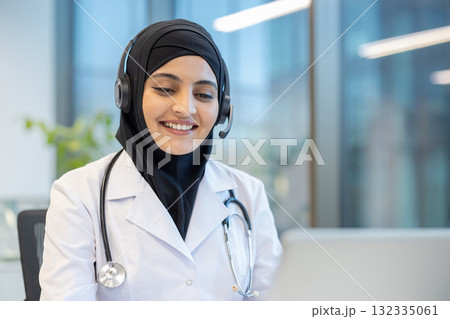 Friendly muslim doctor wearing headset and hijab working on her laptop, providing telehealth services and smiling at a patient on a video call Friendly muslim doctor wearing headset and hijab working on her laptop, providing telehealth services and smiling at a patient on a video call 132335061