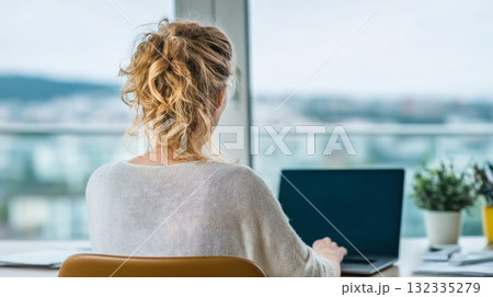 Blonde woman is engaged in remote work at her home office, seated at a desk with a laptop, emphasizing a productive freelance environment 132335279