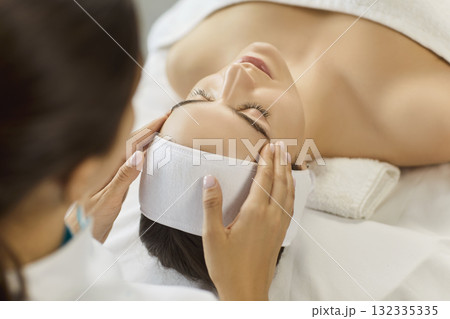 Esthetician performing facial massage for woman client in bright spa treatment room 132335335