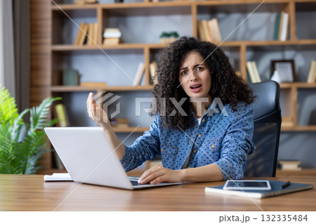 Confused young woman engaging in remote work, experiencing technical difficulties and looking frustrated while sitting at desk with laptop in coworking space Confused young woman engaging in remote work, experiencing technical difficulties and looking frustrated while sitting at desk with laptop in coworking space 132335484