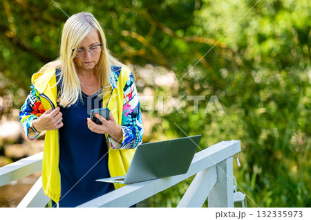 middle age woman at the garden working from home using laptop and speaking on the phone middle age woman at the garden working from home using laptop and speaking on the phone 132335973