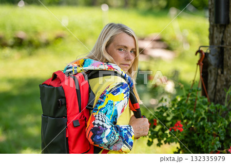 blonde middle-aged woman in bright clothes with a backpack in the park on a sunny day, rear view 132335979