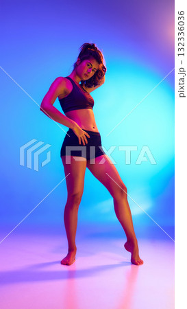 Standing woman in black activewear under neon colored light. Standing woman in black activewear under neon colored light. 132336036