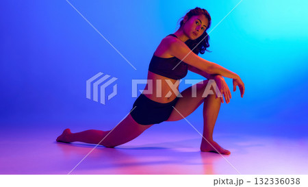 Woman stretching leg on floor in vivid light symbolizing control, flexibility, and active lifestyle 132336038