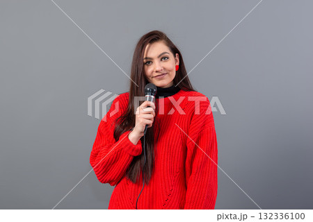 young, emotional brunette with a microphone dressed in a red sweater sings karaoke or says a speech 132336100