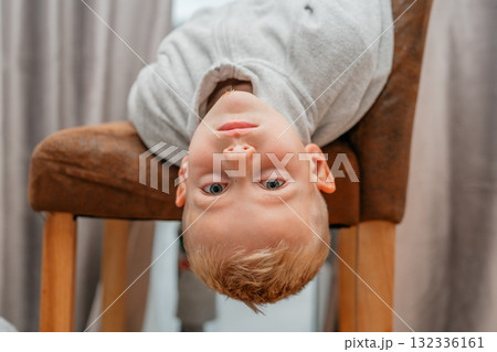 Boy hanging upside down from a chair, smiling playfully candid indoor portrait full of fun and energy Boy hanging upside down from a chair, smiling playfully candid indoor portrait full of fun and energy 132336161