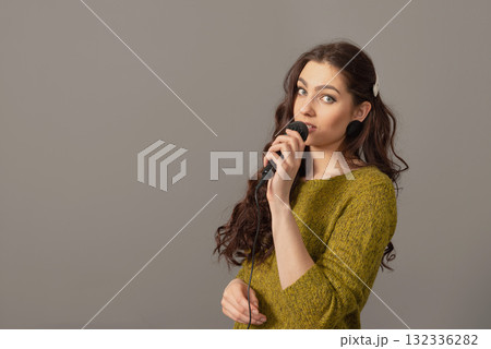attractive teenager woman speaking with a microphone against gray background, conference speaker attractive teenager woman speaking with a microphone against gray background, conference speaker 132336282
