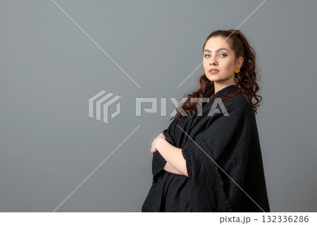 portrait of charming curly-haired woman in a black cloak isolated on a gray background 132336286