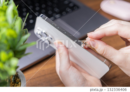 User's hands inserting a SIM ejector tool into a sleek smartphone, preparing to open the SIM card tray for mobile connectivity or device activation User's hands inserting a SIM ejector tool into a sleek smartphone, preparing to open the SIM card tray for mobile connectivity or device activation 132336406