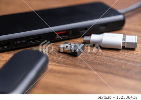 Black USB-C multiport hub, HDMI port, wireless dongle, and USB-C adapter on wooden desk, providing expanded connectivity for modern devices 132336418