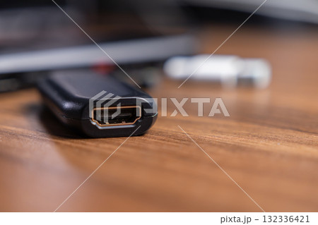 Black HDMI adapter with an open golden port lying on a warm wooden surface, essential for multimedia connectivity, home entertainment, and modern computing technology 132336421