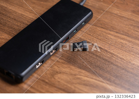 Black USB hub with multiple ports, positioned beside a tiny wireless dongle, essential for expanding modern digital workspace connectivity and device peripherals 132336423