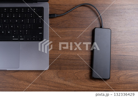 Modern laptop connected to a black external drive on a wooden desk, symbolizing crucial data backup, digital storage, and portable file management 132336429