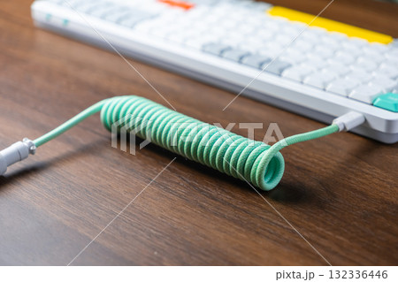Mint green coiled braided USB cable connected to a modern mechanical keyboard on a wooden desk, enhancing desktop aesthetics for work or gaming 132336446