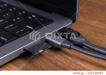 Modern gray laptop on a wooden desk with an inserted SD card, connected USB-C hub, and HDMI cable, for versatile digital data transfer and external display 132336465