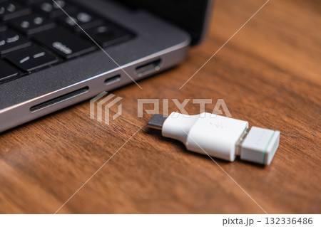 White USB-C USB-A adapter on wood desk near open laptop, offering versatile connectivity and rapid data transfer for electronic devices in digital workspaces 132336486