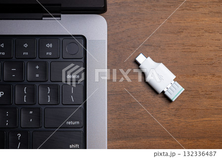 Compact white USB-C to USB-A adapter resting on a wooden office desk near a modern laptop, enabling crucial versatile digital connectivity and data transfer 132336487