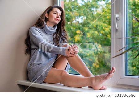 young sensual millennial woman looking through the window sitting on a windowsill 132336686