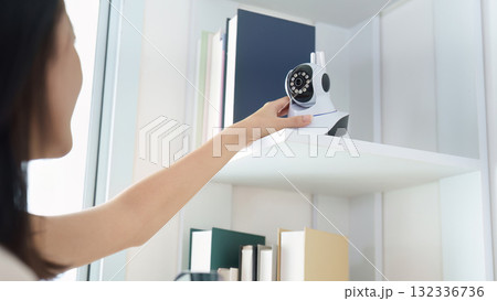 Smart Home. Close-up of woman adjusting security camera on shelf. 132336736