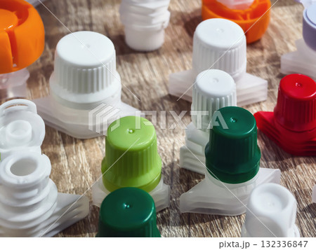 Collection of colorful plastic bottle caps scattered on a wooden surface during bright afternoon light 132336847