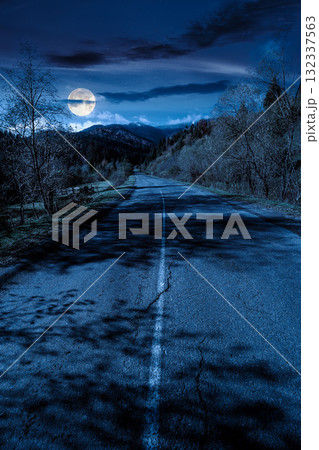road through mountain landscape of in autumn at night. forest in fall colors under dark sky in full moon light. snow covered peak in the distance. scenic view of rural valley 132337563