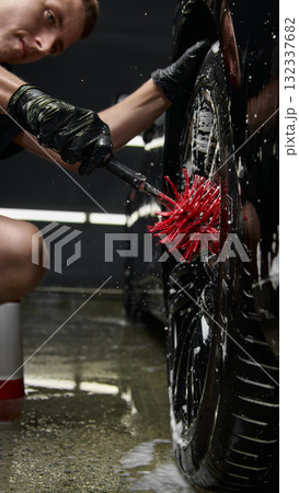 Focused worker cleaning wheel rim with red brush at car detailing center 132337682