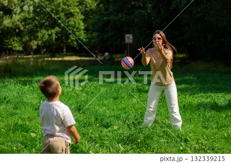 Mom and kid play ball together in nature during summer holidays. Playing ball with son in park. Catching ball. 132339215