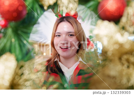 Christmas Cheer. Young woman smiling through festive decorations. Christmas Cheer. Young woman smiling through festive decorations. 132339303