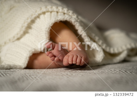 Cute baby feet peeking out from a cozy knitted blanket during a peaceful moment at home 132339472