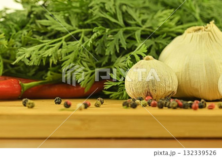 A bulb of garlic, red chili peppers, four-color pepper, and carrot tops on a wooden cutting board. The concept of cooking and vegetables in the home. Garlic - Allium sativum is a species of bulbous 132339526