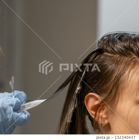 Hair coloring process in a salon with a stylist applying foil highlights to a customers hair Hair coloring process in a salon with a stylist applying foil highlights to a customers hair 132340437